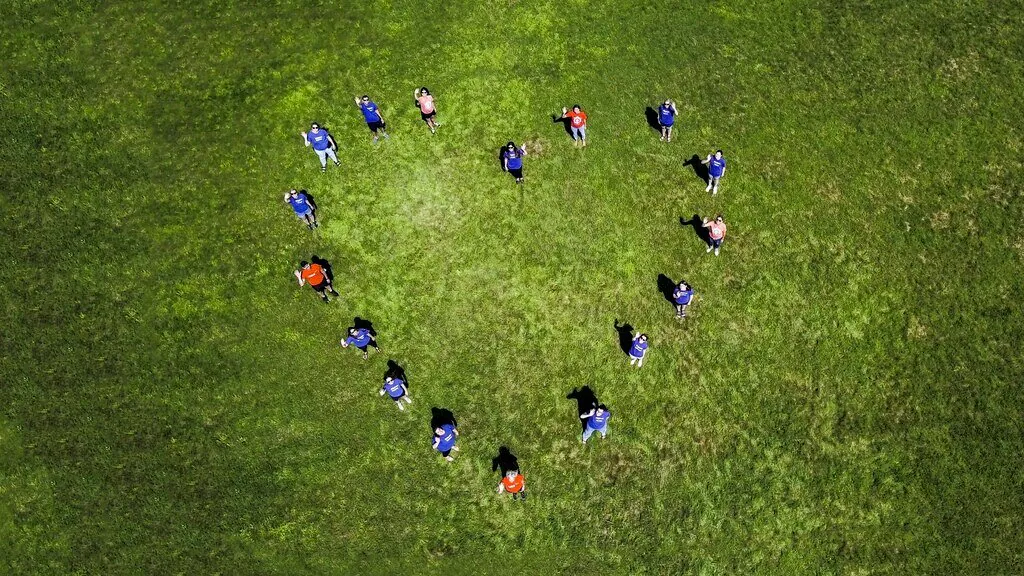 Des employés de 3M, photographiés d’en haut, se tiennent en formation de cœur sur l’herbe