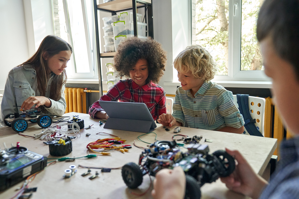 Trois jeunes regardent une tablette pendant qu’un autre étudiant assemble un véhicule robotisé.